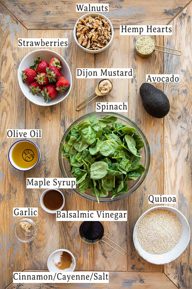 Ingredients for avocado strawberry spinach salad recipe on a wood table.
