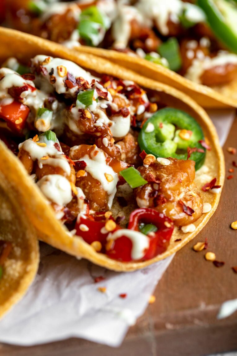 Angled close up of Kung Pao Shrimp Tacos in corn tortillas with Jalapeño Sauce.