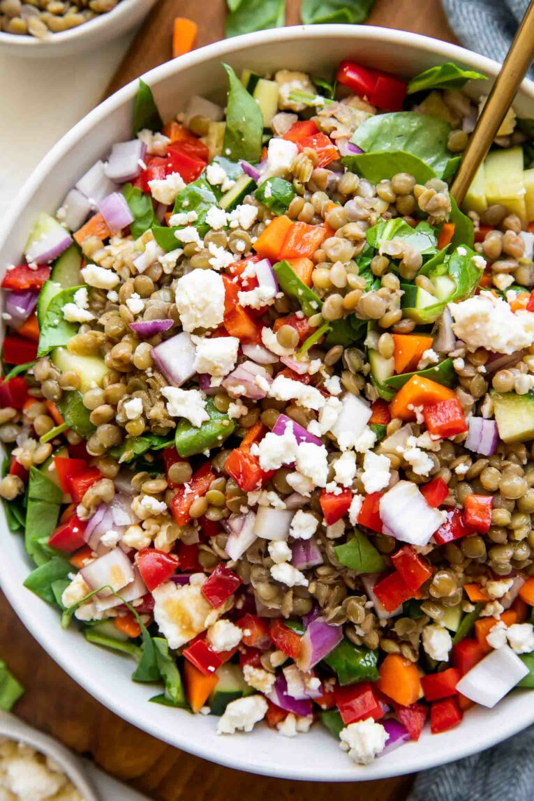 Close up of healthy spring salad with chopped veggies, cooked lentils, feta, and lemon balsamic dressing.