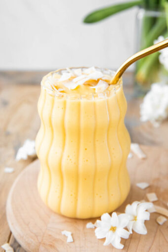 Angled photo of Healthy Mango Banana Smoothie with coconut chips on top.