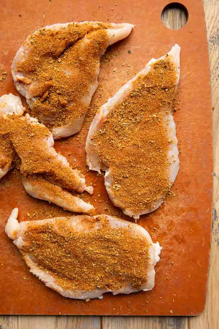 Chicken with barbecue seasoning rub on a cutting board.