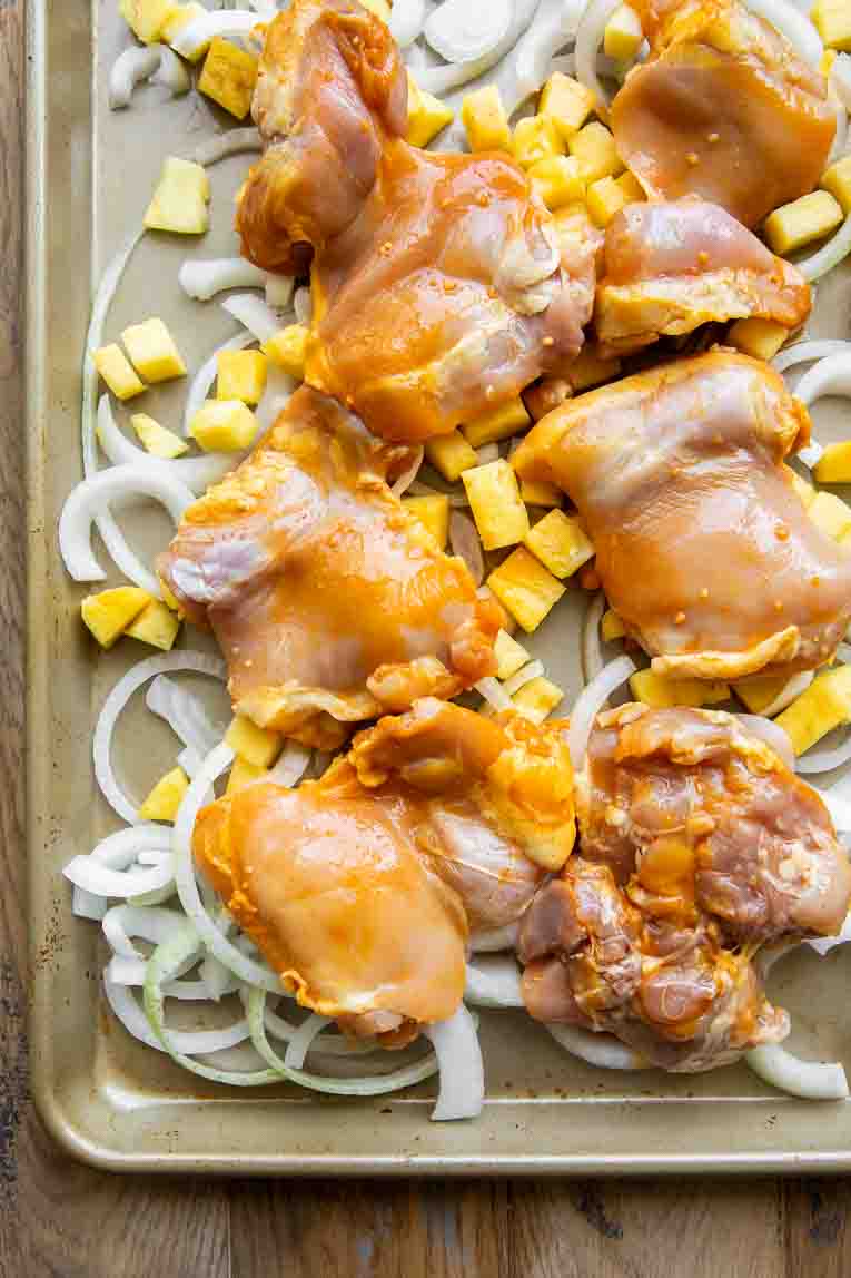 Onions, pineapples, and marinated chicken on a baking sheet.