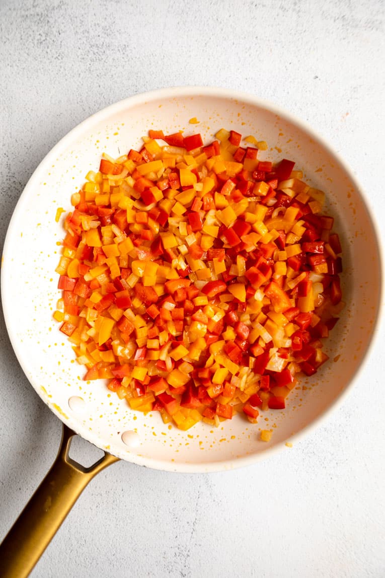Peppers, onions, and seasoning being sautéed for baked empanadas.
