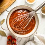 Homemade BBQ Sauce Recipe in a bowl with a whisk and ingredients.