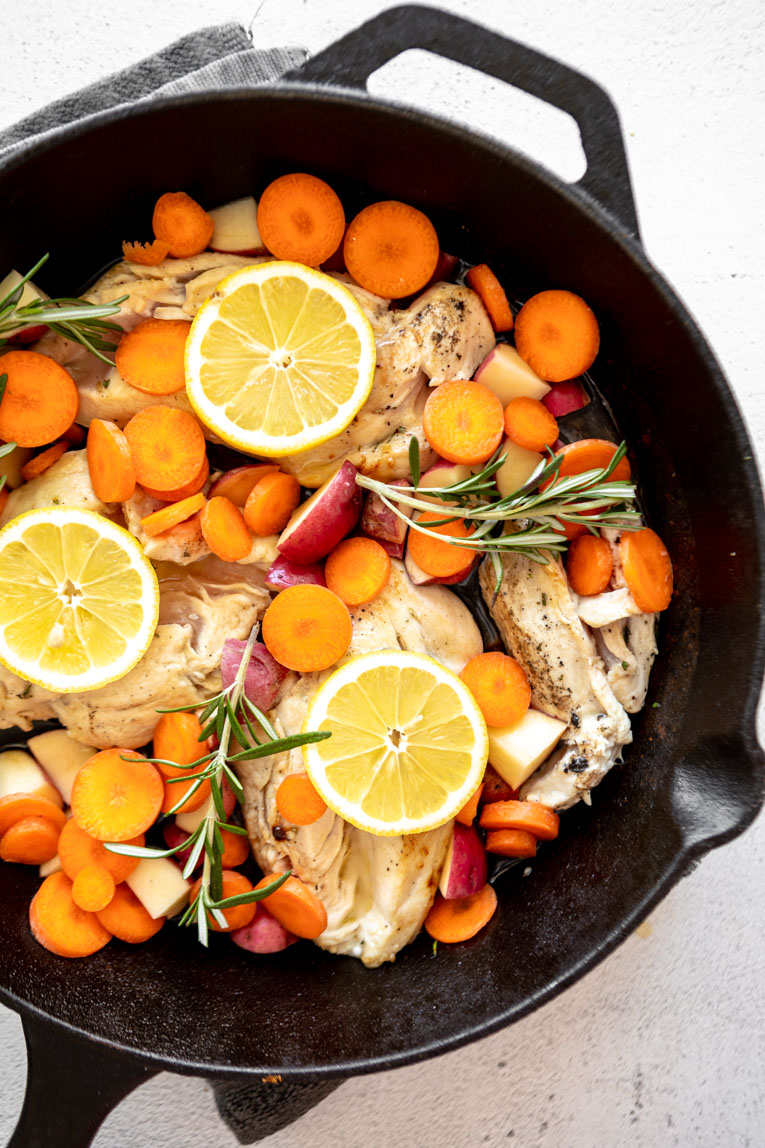 Browned chicken and veggies with rosemary and lemon in a cast iron skillet.
