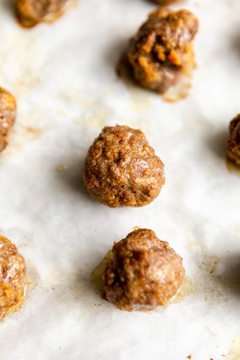Baked meatballs cooling on a baking sheet.