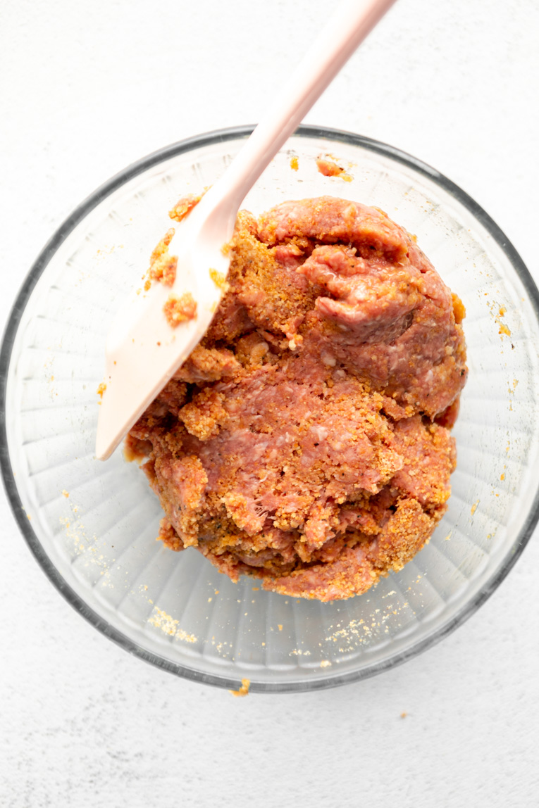 Ground beef and seasoning with egg in a large mixing bowl.