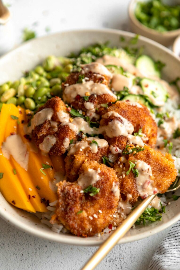 Fried shrimp in a bowl with rice, veggies, mango, and creamy sauce.
