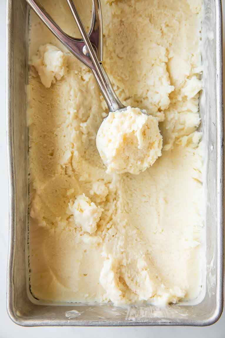 Frozen Lemon Ice Cream in an ice cream tin with a scoop.