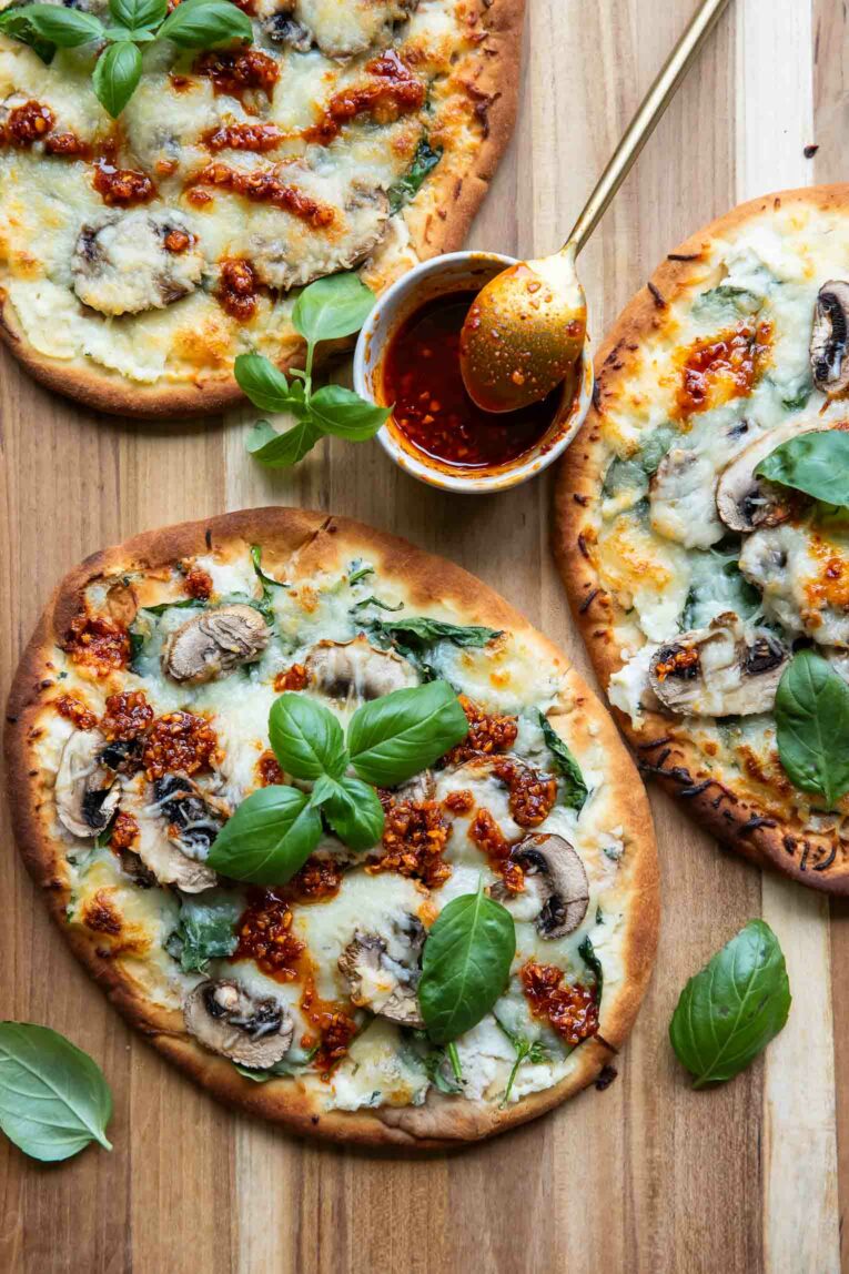 Individual naan pizzas with chili crunch on a wood board.