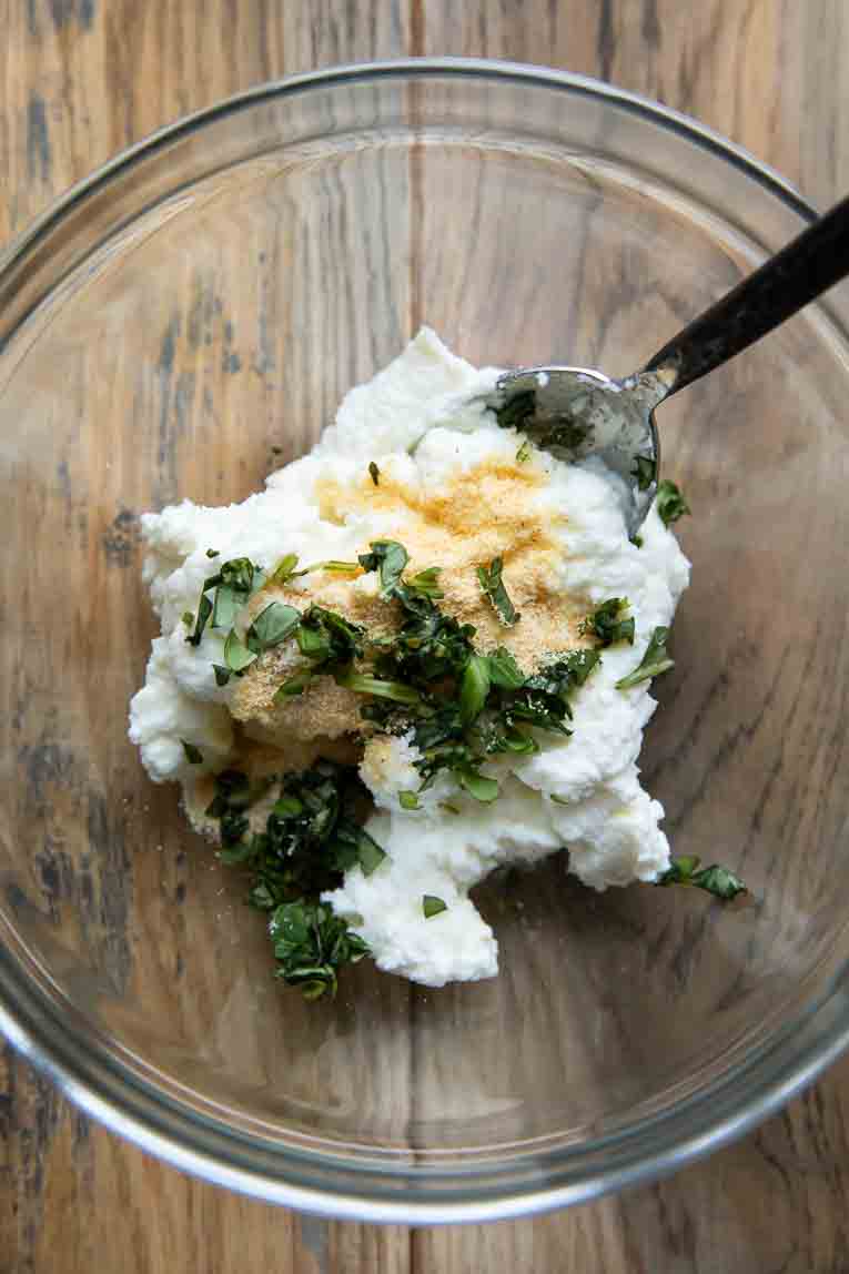 Ricotta being mixed with garlic seasoning in a bowl.