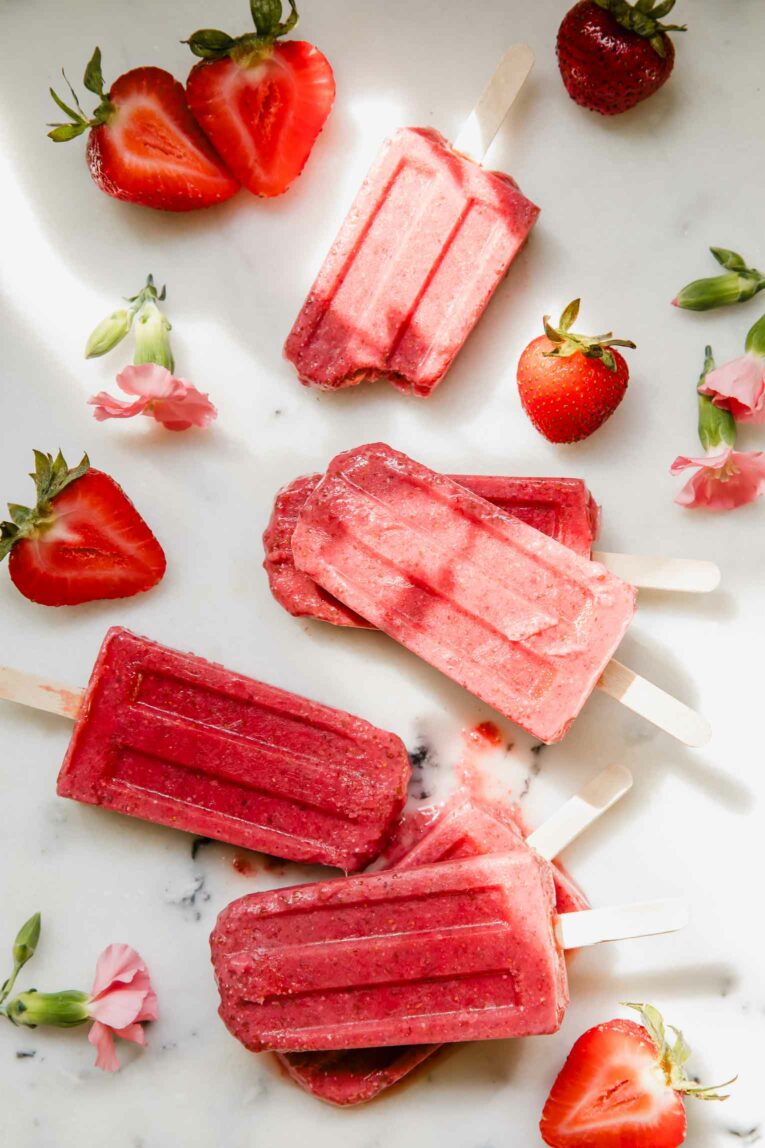 Strawberry popsicles recipe on a marble countertop with flowers.