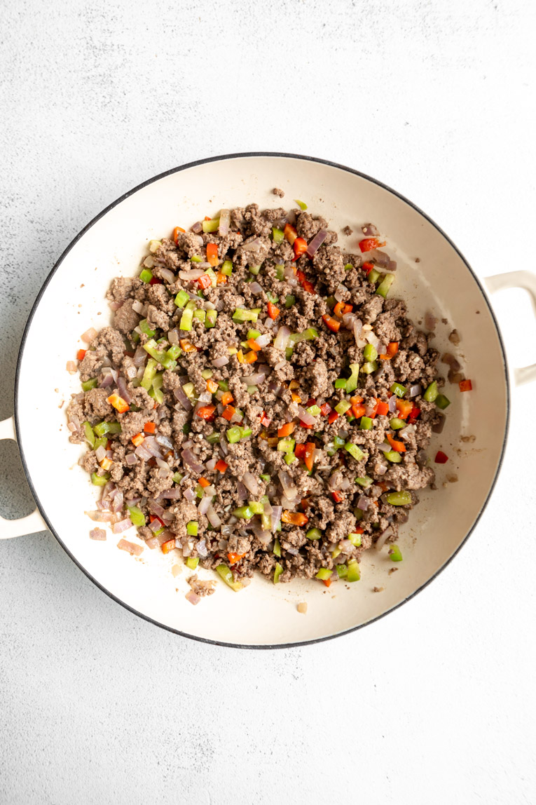 Ground beef and bell peppers with onions in a skillet.