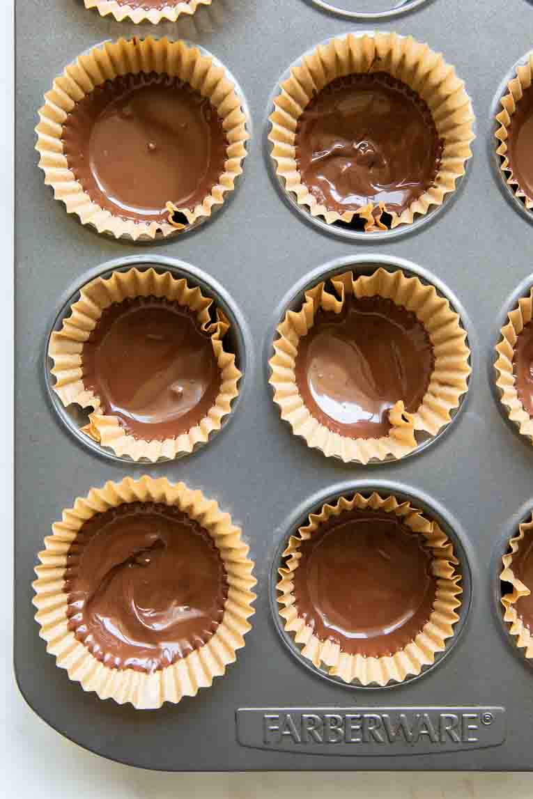 Bottom layer of chocolate for peanut butter cups in a muffin tin.