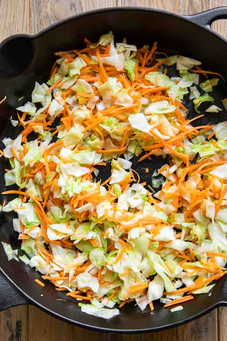 Cabbage and carrots being cooked in a skillet.