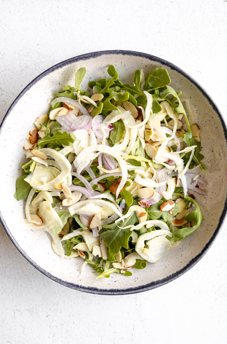 Arugula, parmesan, red onion, and other salad ingredients in a bowl.