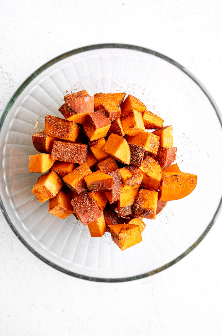 Cubed sweet potatoes tossed in oil and seasoning in a bowl.