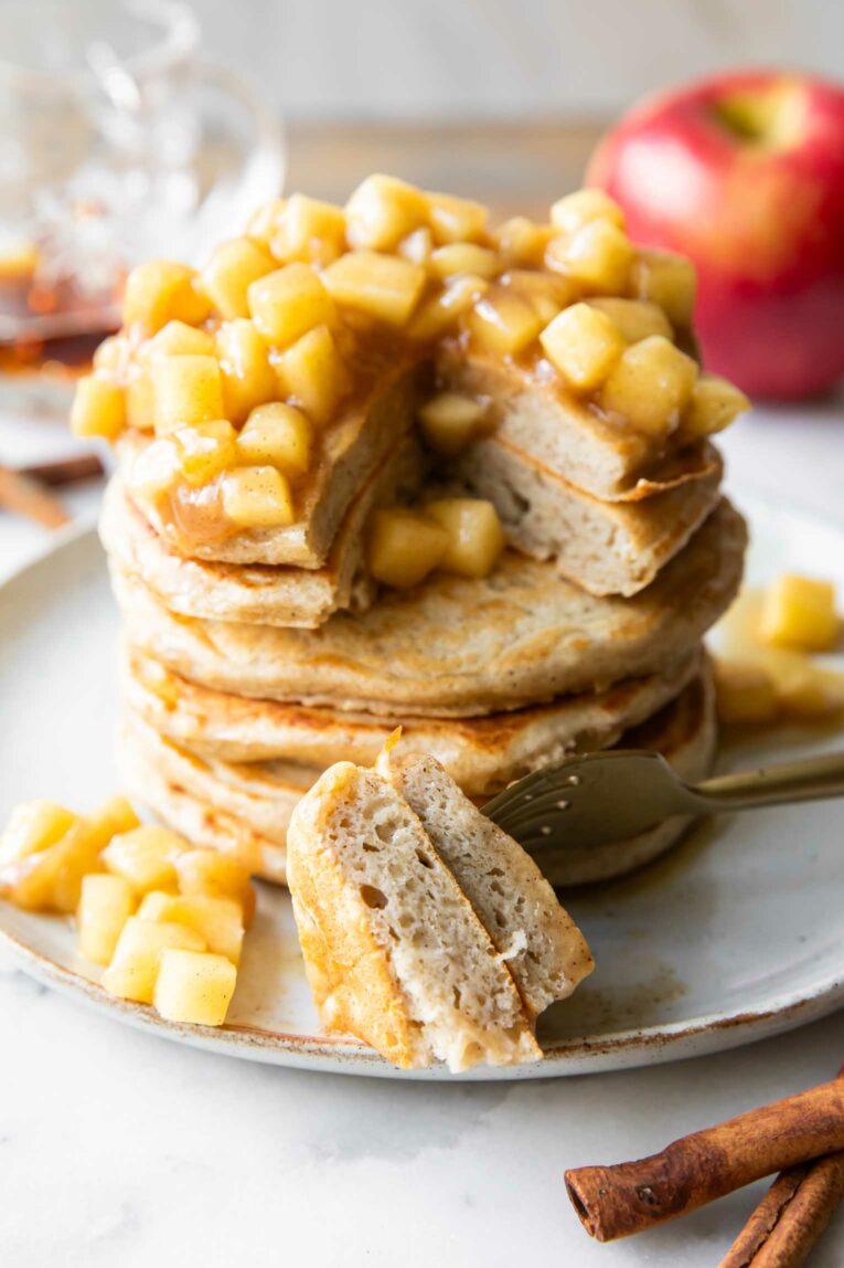Angled photo of stack of apple pancakes with a bite taken out.
