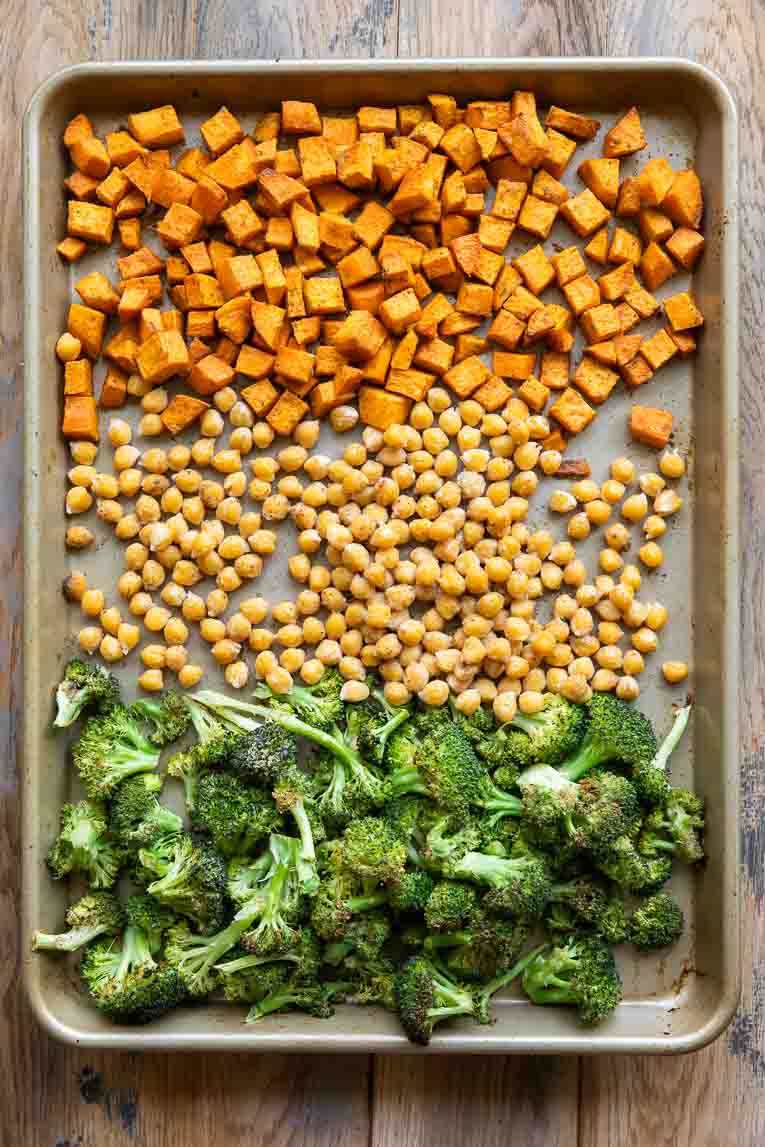 Top shot photo of broccoli, chickpeas, and sweet potatoes roasting on a sheet pan.