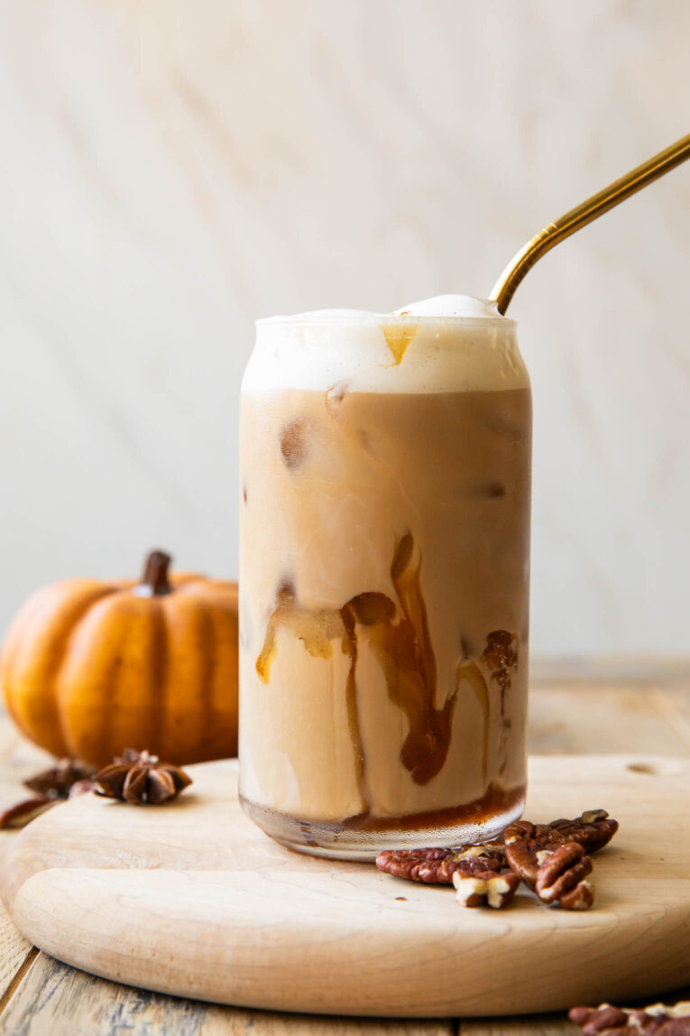 Iced Pecan Crunch Oatmilk Latte in a glass with a pumpkin in the background.