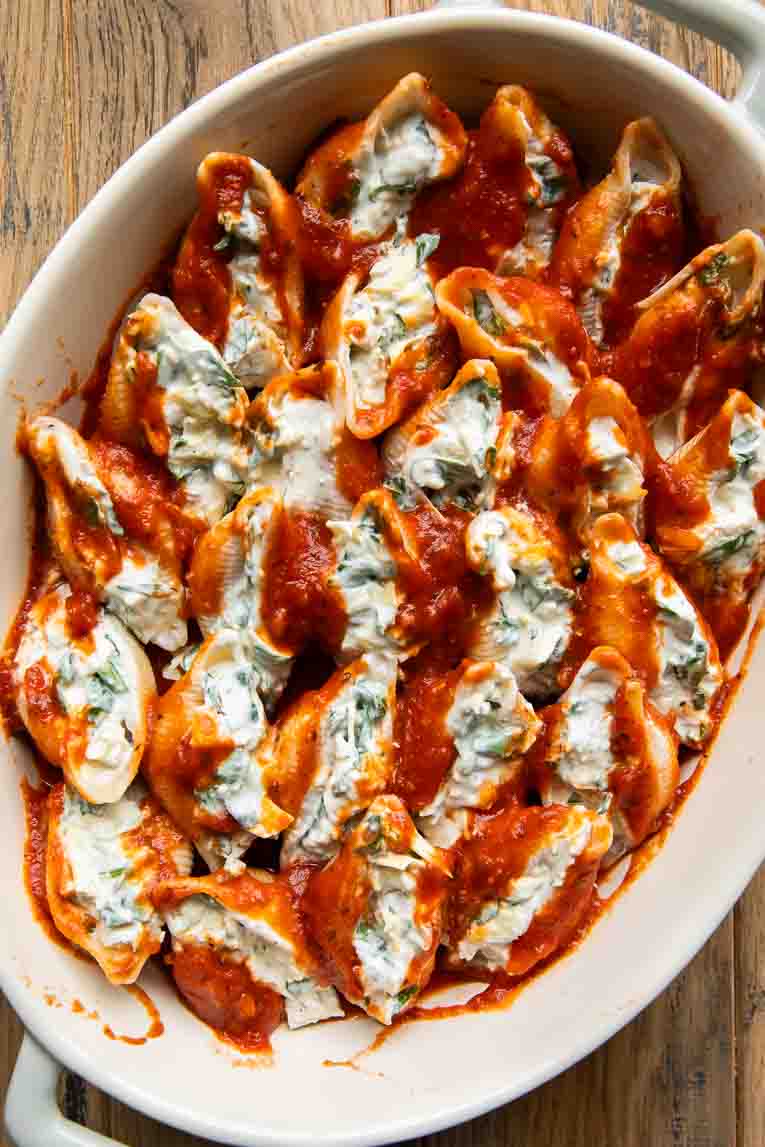 Chicken Spinach Artichoke Stuffed Shells with red sauce in a baking dish.