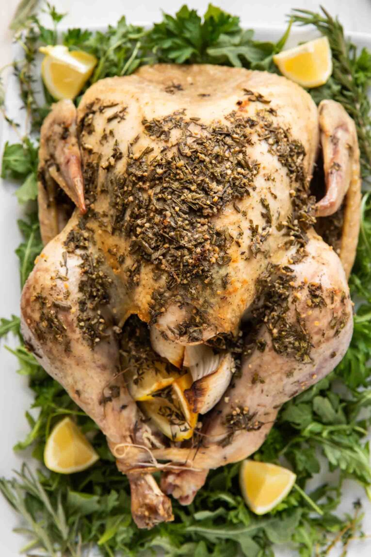 Thanksgiving turkey on a serving platter with greens, herb butter, and lemon slices.