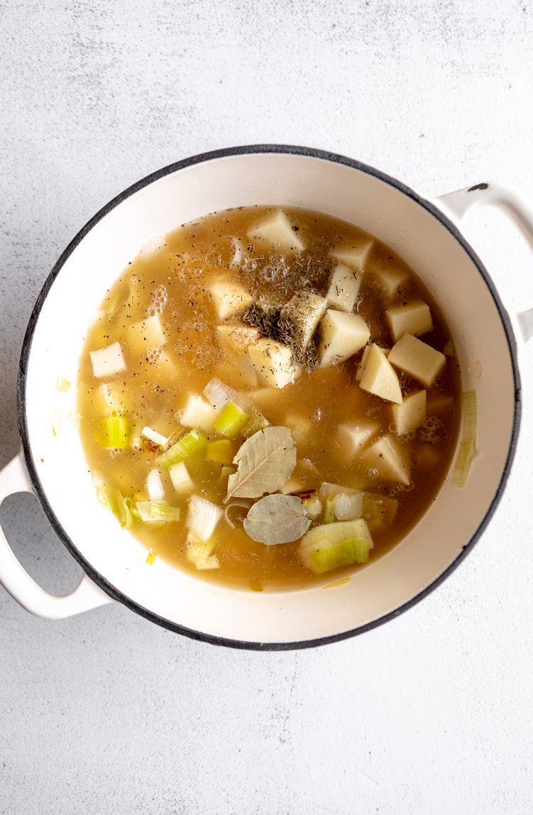 Leeks, onions, and potatoes simmering in broth in a dutch oven.