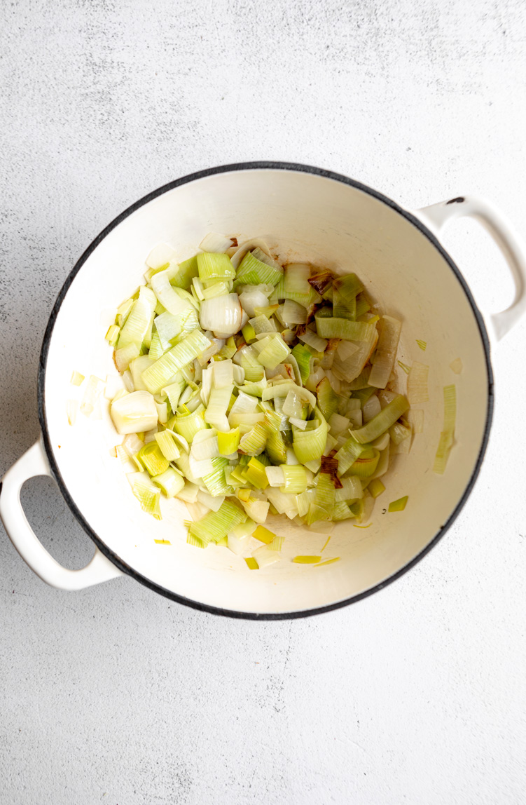 Leeks and onions being sautéed in butter in a Dutch oven.