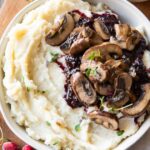 Slow Cooker Mashed Potatoes in a bowl with cranberry mushroom sauce.