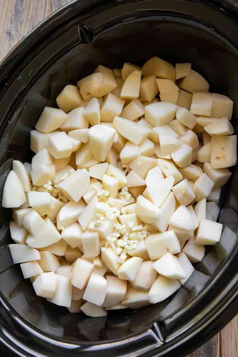 Cubed potatoes with water and garlic in a crockpot.