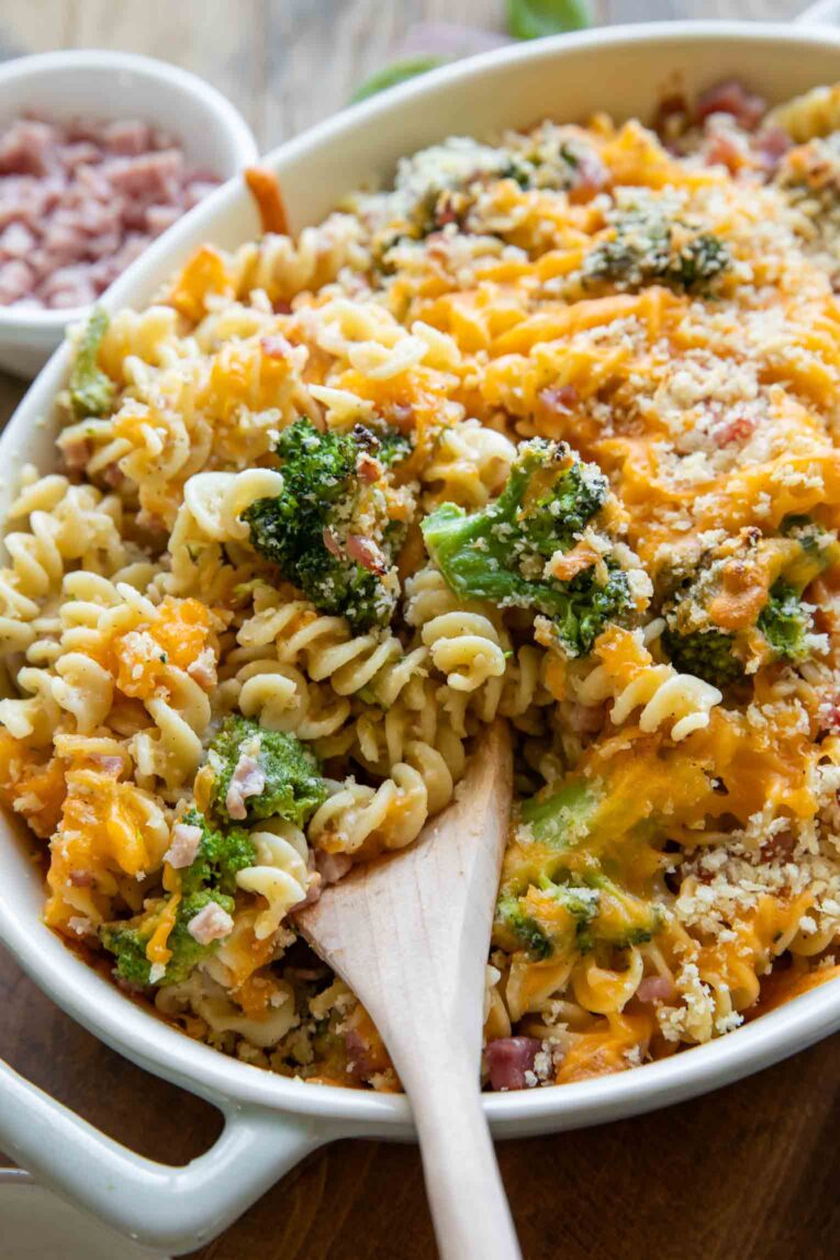 Angled photo of Broccoli Cheddar Ham Pasta Casserole with wooden spoon.