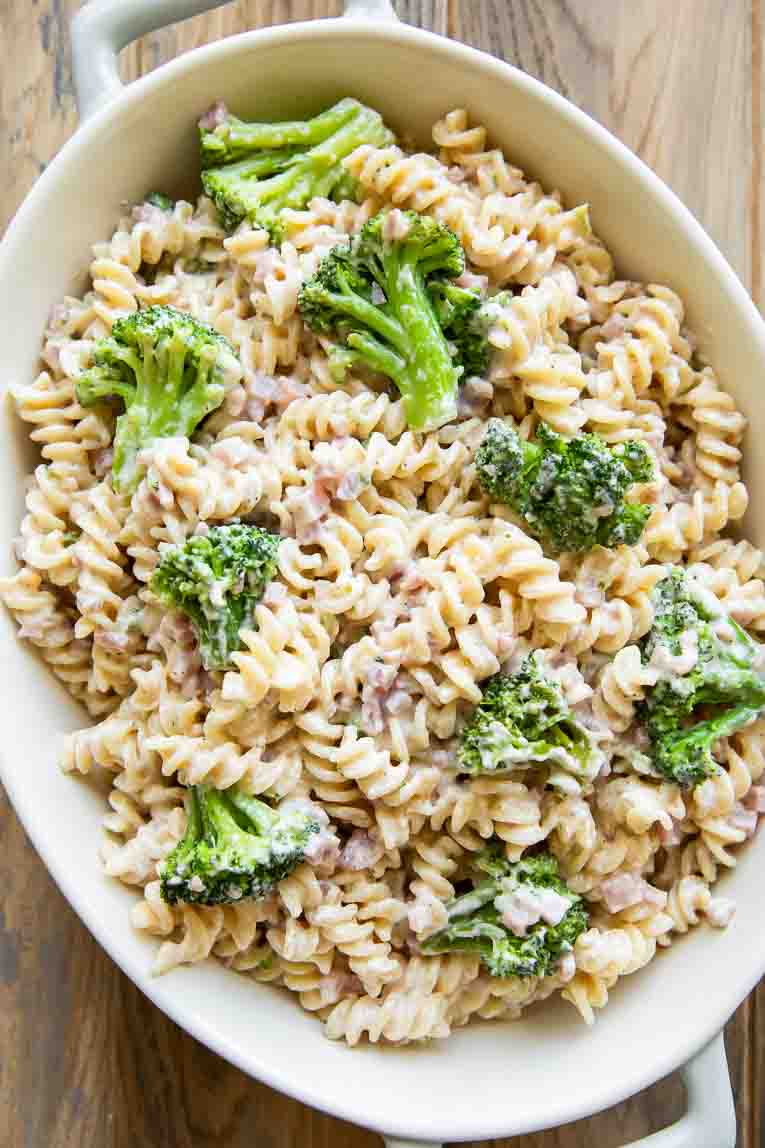 Ingredients for a Broccoli Cheddar Ham Pasta Casserole in a casserole dish.