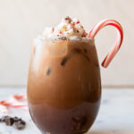 Iced Peppermint Mocha in a glass with whipped cream and candy cane.