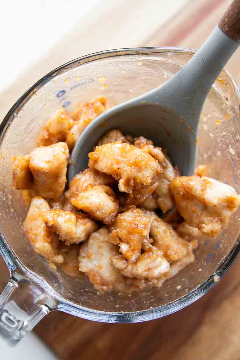 Chicken being mixed with orange honey sauce in a bowl.