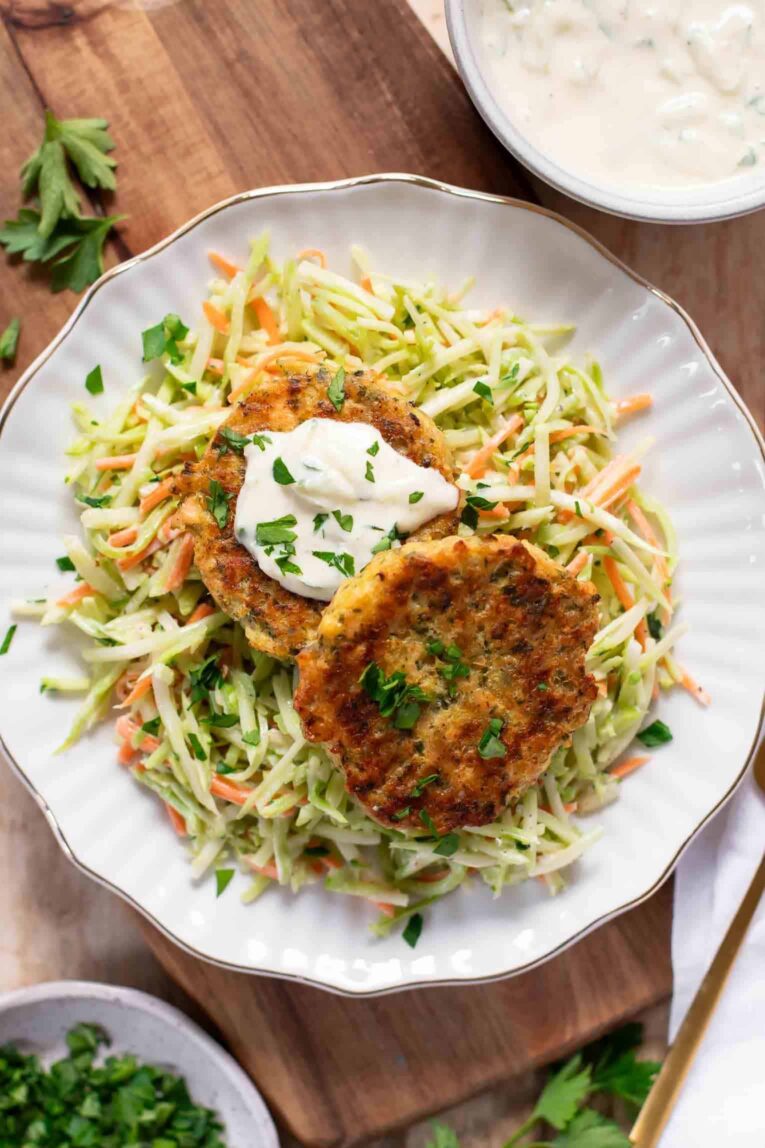 Easy Salmon Patties recipe on a plate with broccoli slaw and Tzatziki sauce.
