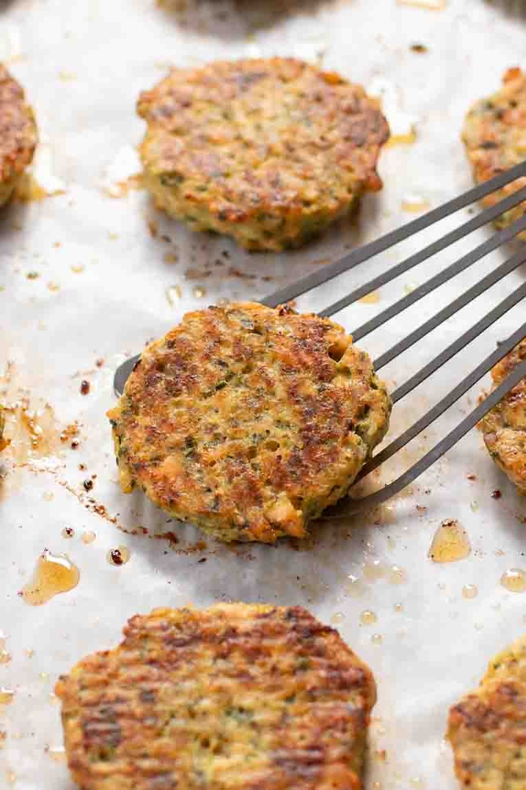 Salmon Patties being lifted off of a baking sheet.