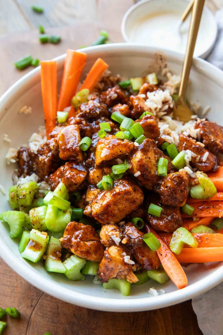Angled photo of buffalo chicken in a bowl with carrots, celery, and rice.