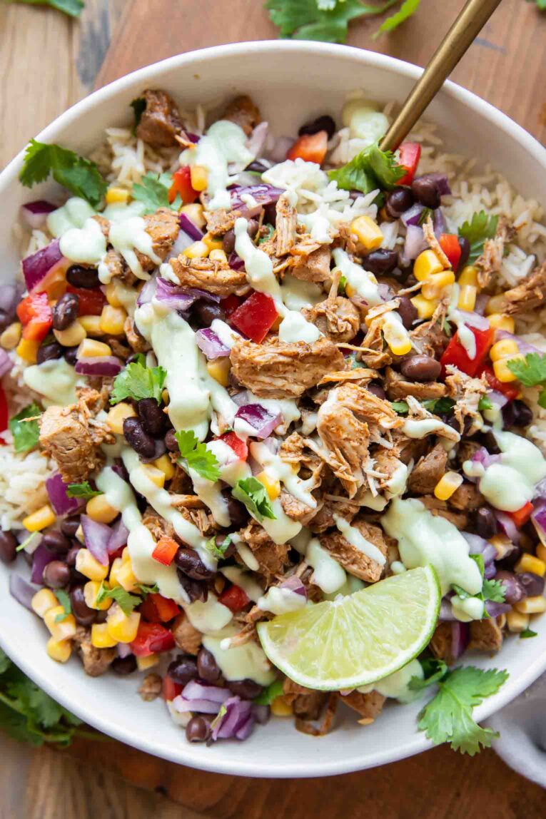 Top shot of easy Carnitas bowl with rice, pork, beans, corn, salsa, and dressing.