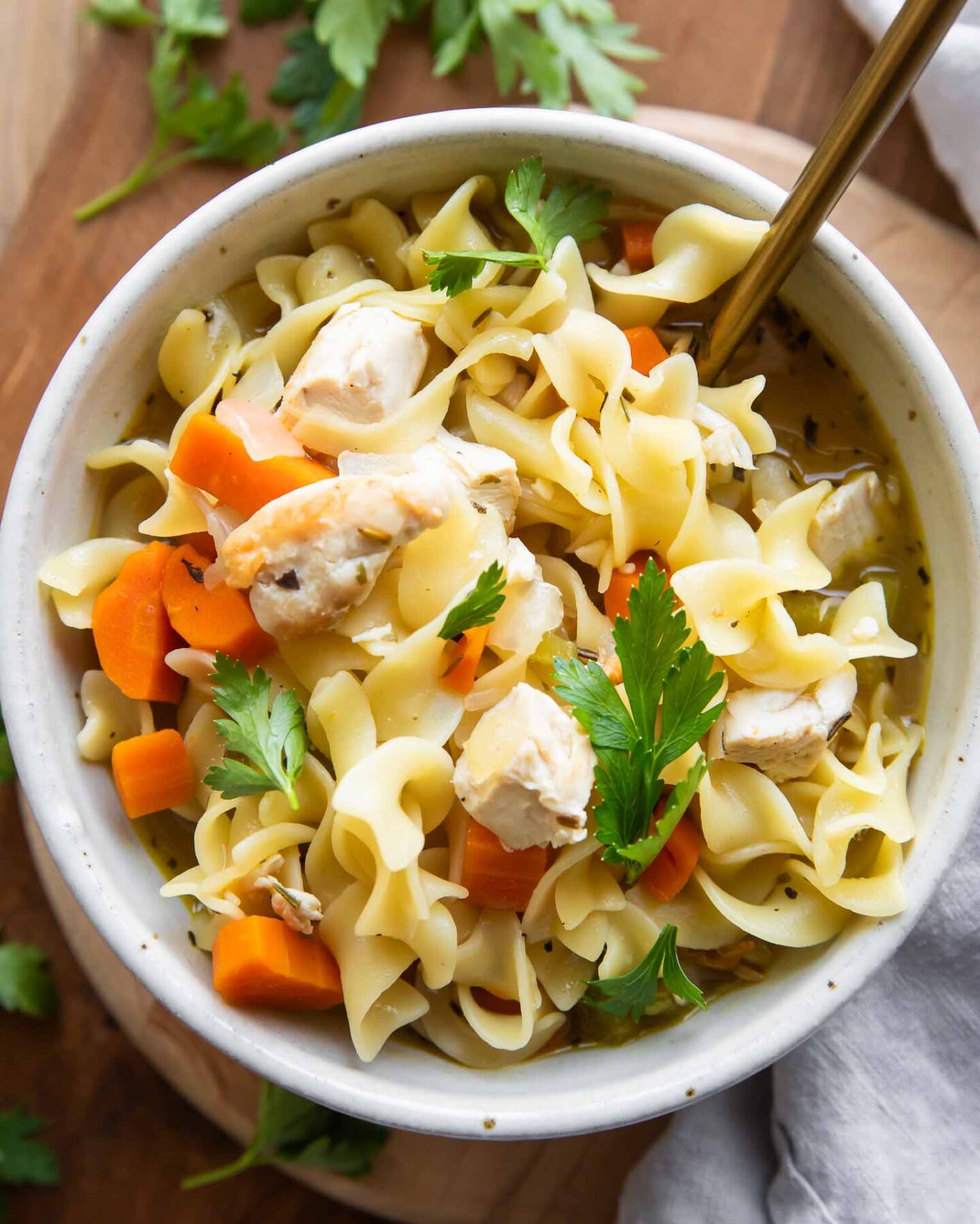 Chicken Noodle Soup in a bowl on a wood cutting board.