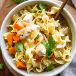 Chicken Noodle Soup in a bowl on a wood cutting board.