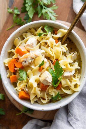 Chicken Noodle Soup in a bowl on a wood cutting board.