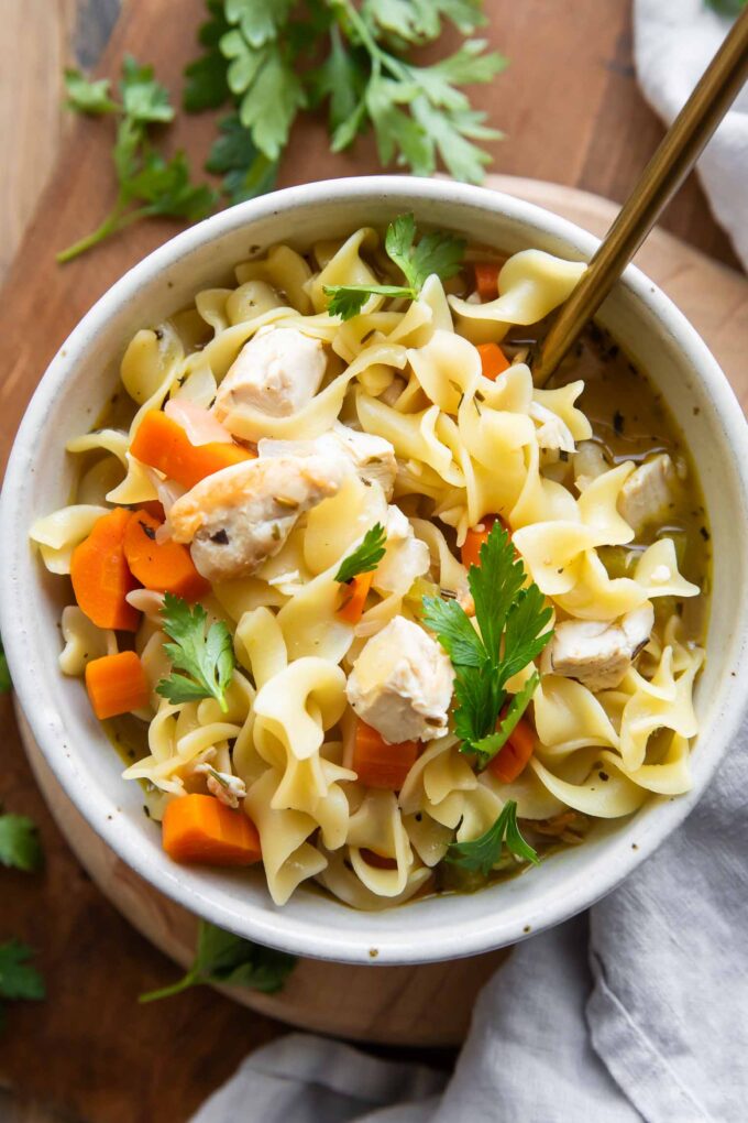 Chicken Noodle Soup in a bowl on a wood cutting board.