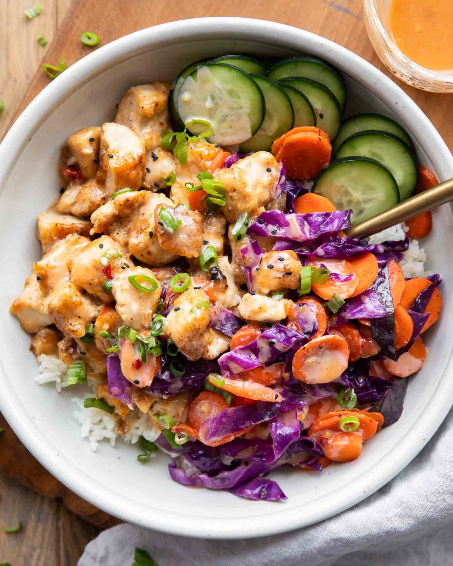 Bang bang chicken recipe in a bowl with rice, veggies, and sauce.