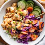 Bang bang chicken recipe in a bowl with rice, veggies, and sauce.