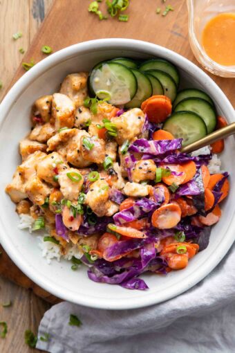 Bang bang chicken recipe in a bowl with rice, veggies, and sauce.
