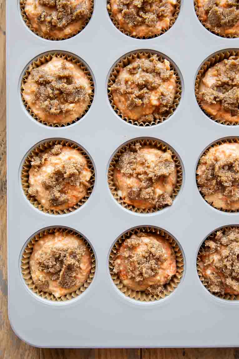 Streusel topping over healthy Carrot Cake Muffin batter in a muffin tin.