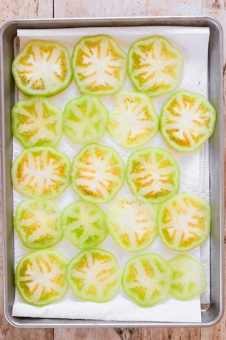 Sliced green tomatoes on a baking sheet.