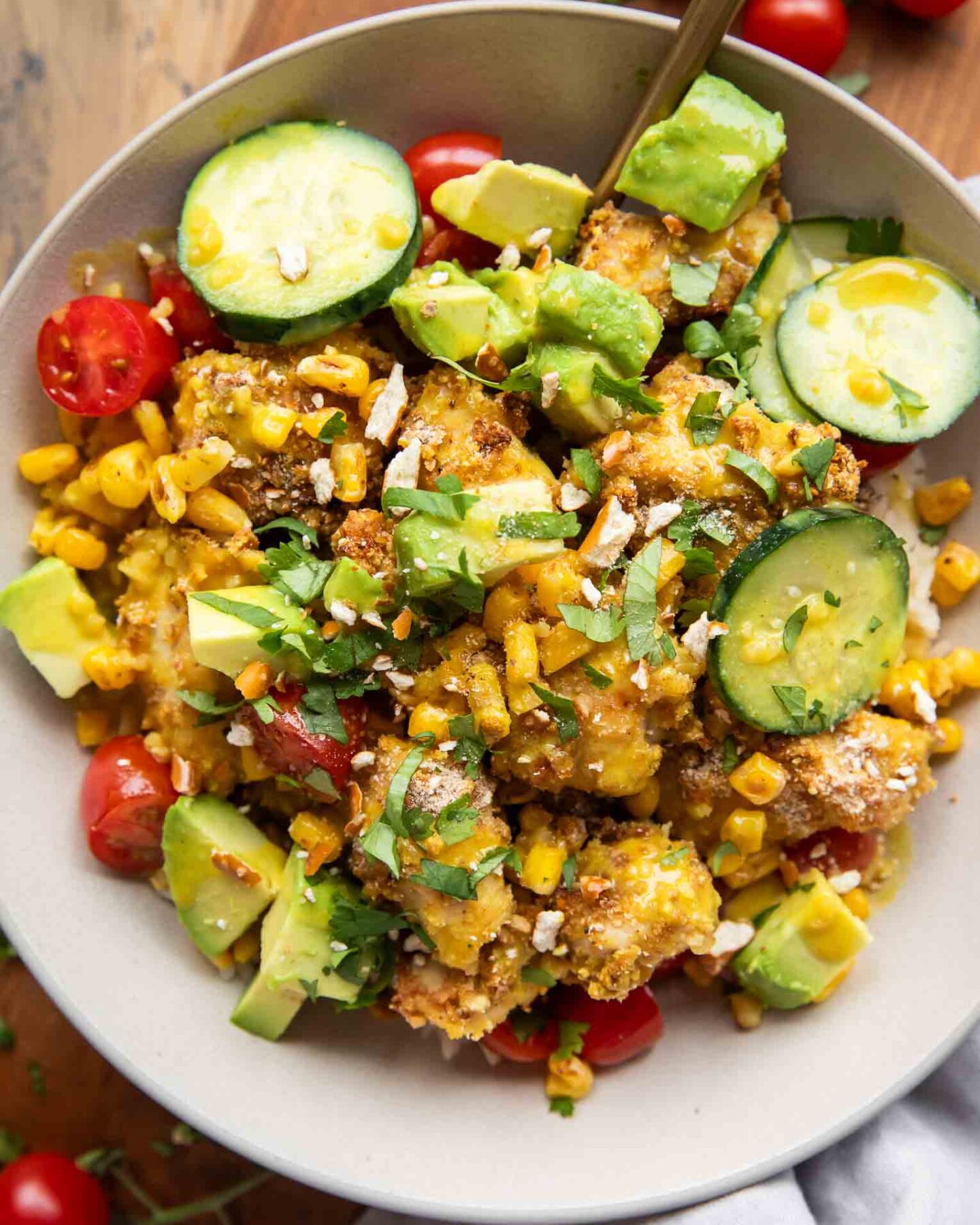 Bowl of honey mustard chicken with pretzel breading, rice, cucumbers, and corn.