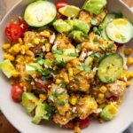 Bowl of honey mustard chicken with pretzel breading, rice, cucumbers, and corn.
