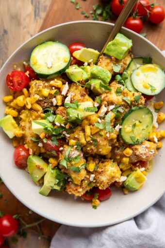 Bowl of honey mustard chicken with pretzel breading, rice, cucumbers, and corn.